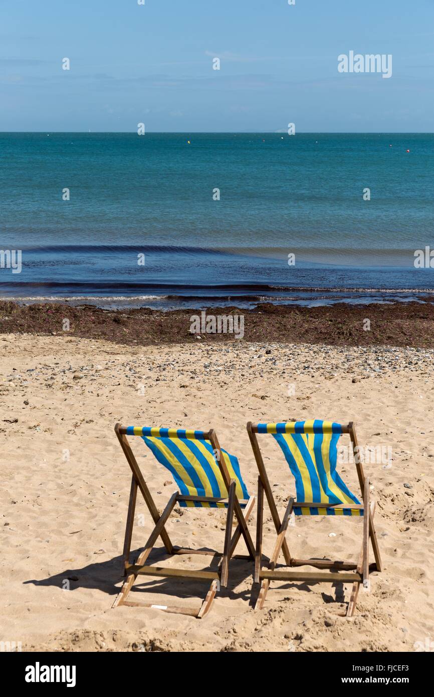 Two blue and white striped beach chairs on the sand beach with its back ...