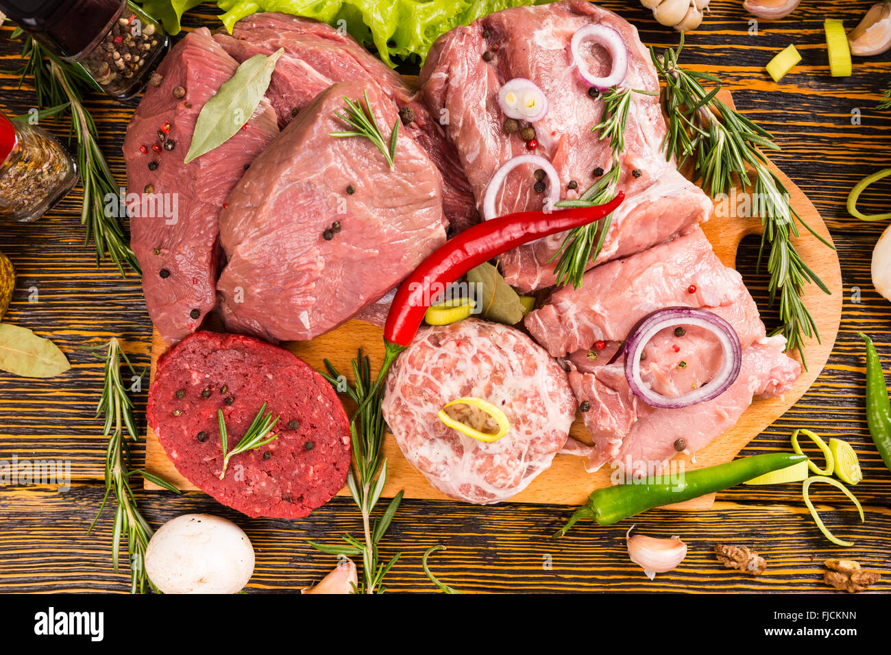 First person perspective of and abundance of raw beef and pork with seasonings surrounded by wood grain table Stock Photo