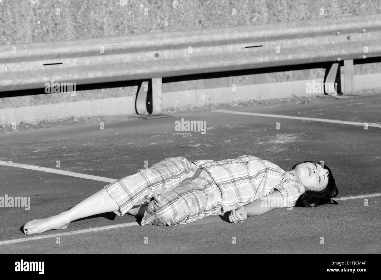 July 2015 - Young woman playing dead in her pajamas on top of a multi storey car park Stock Photo