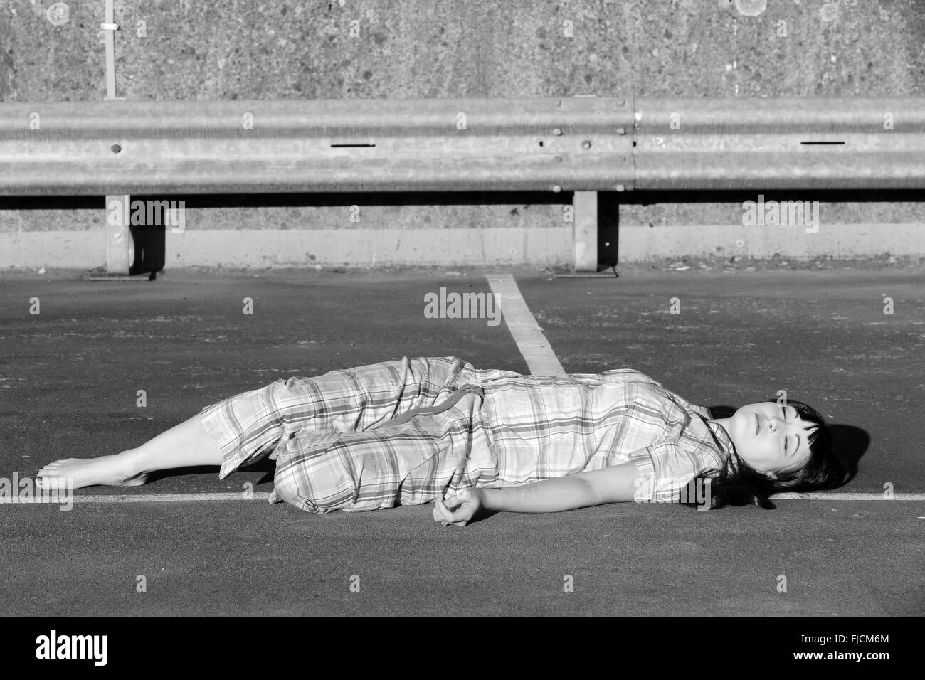 July 2015 - Young woman playing dead in her pajamas on top of a multi storey car park Stock Photo