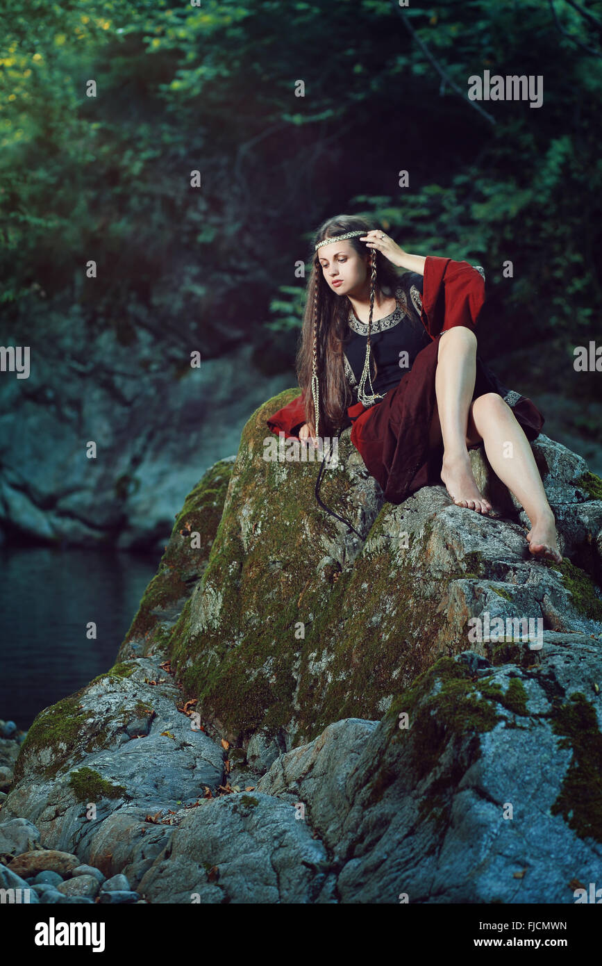 Medieval young lady posing on a stream rock . Historical and fantasy Stock Photo