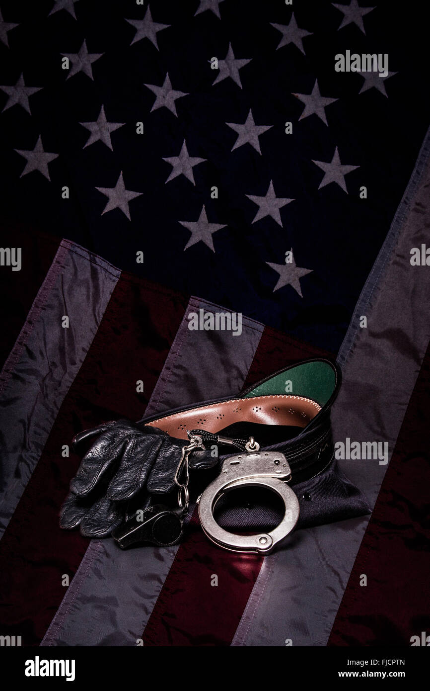 A police hat with leather gloves, whistle, and handcuffs on an American flag background. Stock Photo