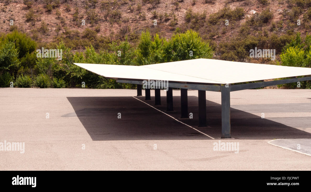 Large empty carport against desert shrubs, casting shadow. Stock Photo