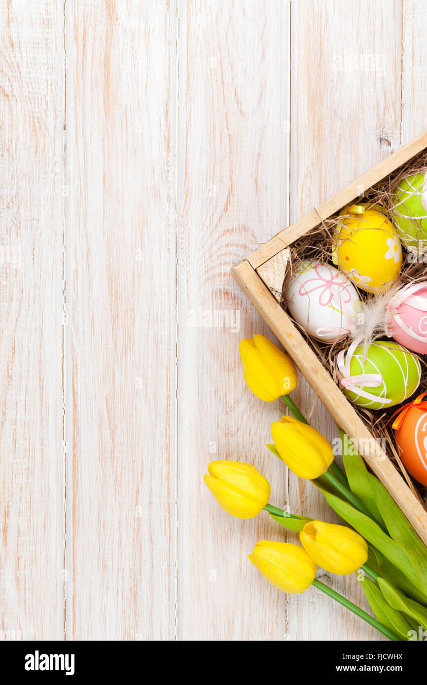 Easter background with colorful eggs and yellow tulips over white wood ...