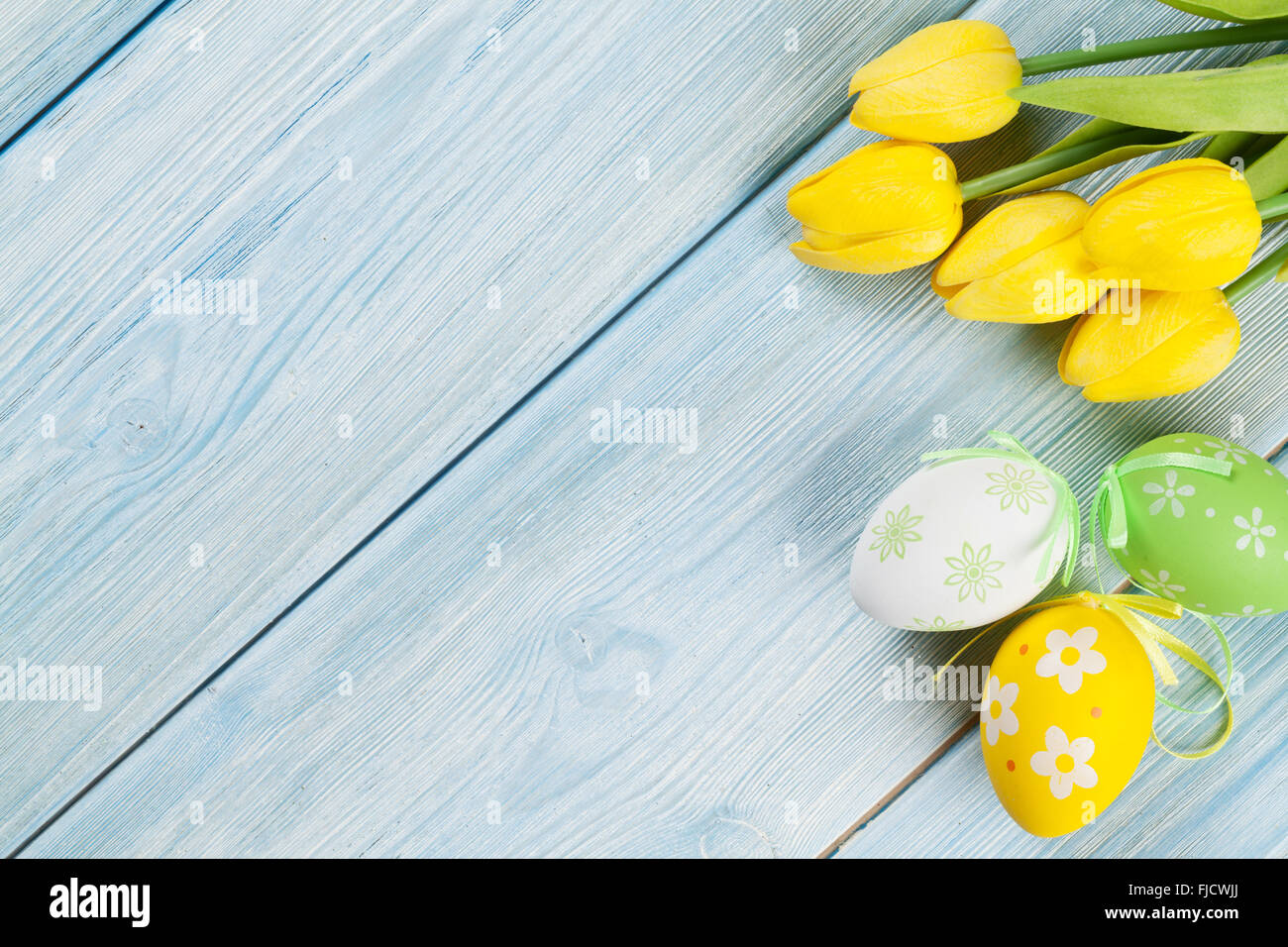 Easter eggs and yellow tulips over wooden background with copy space ...