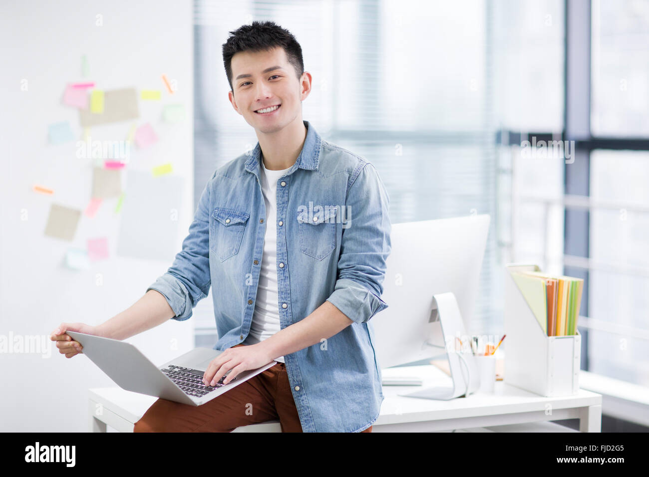 Young Chinese man using laptop in office Stock Photo