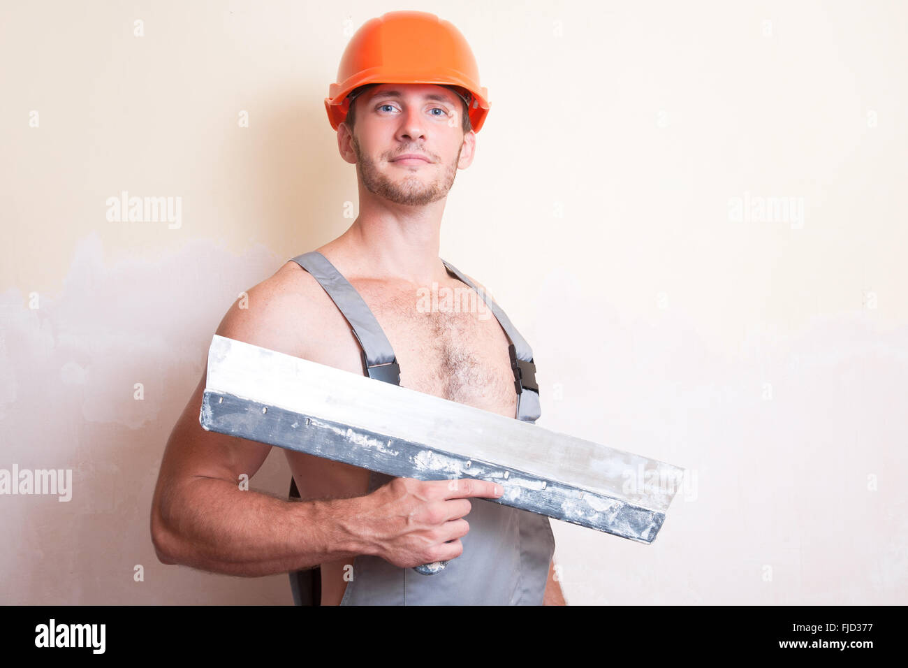 A man in overalls and helmet with a large spatula Stock Photo