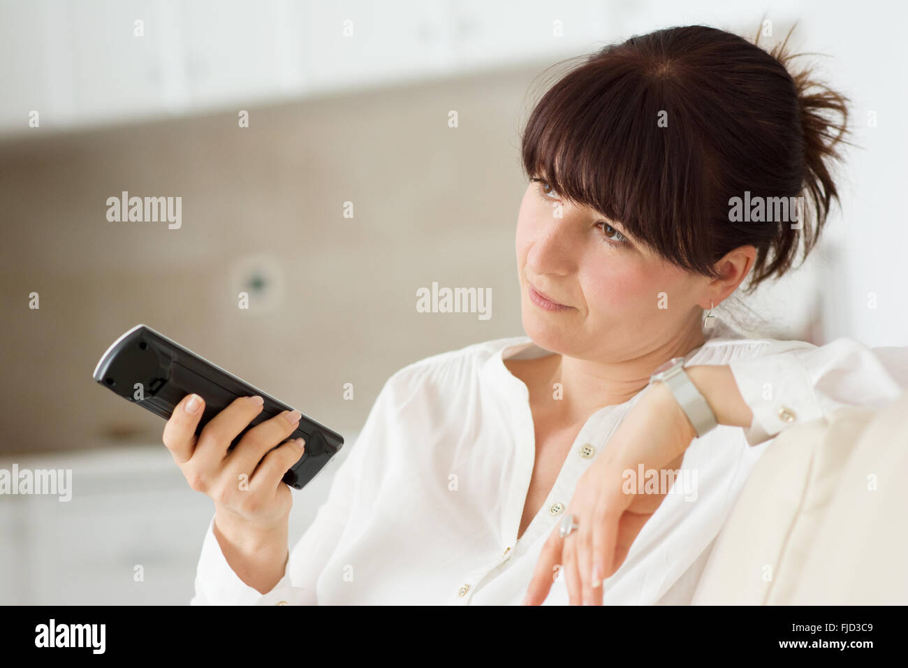 Woman in home watching television and changing channels with remote control Stock Photo