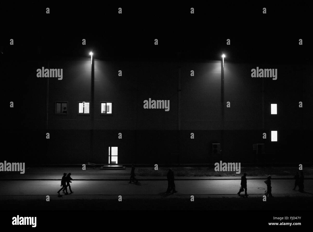 People walking on the night street with streetlights against the building with luminous windows Stock Photo