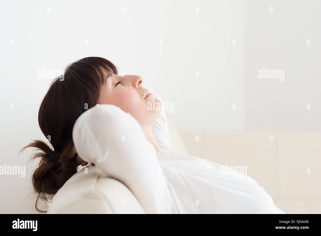 Woman relaxing in her home on a couch with arms behind her neck and closed eyes Stock Photo