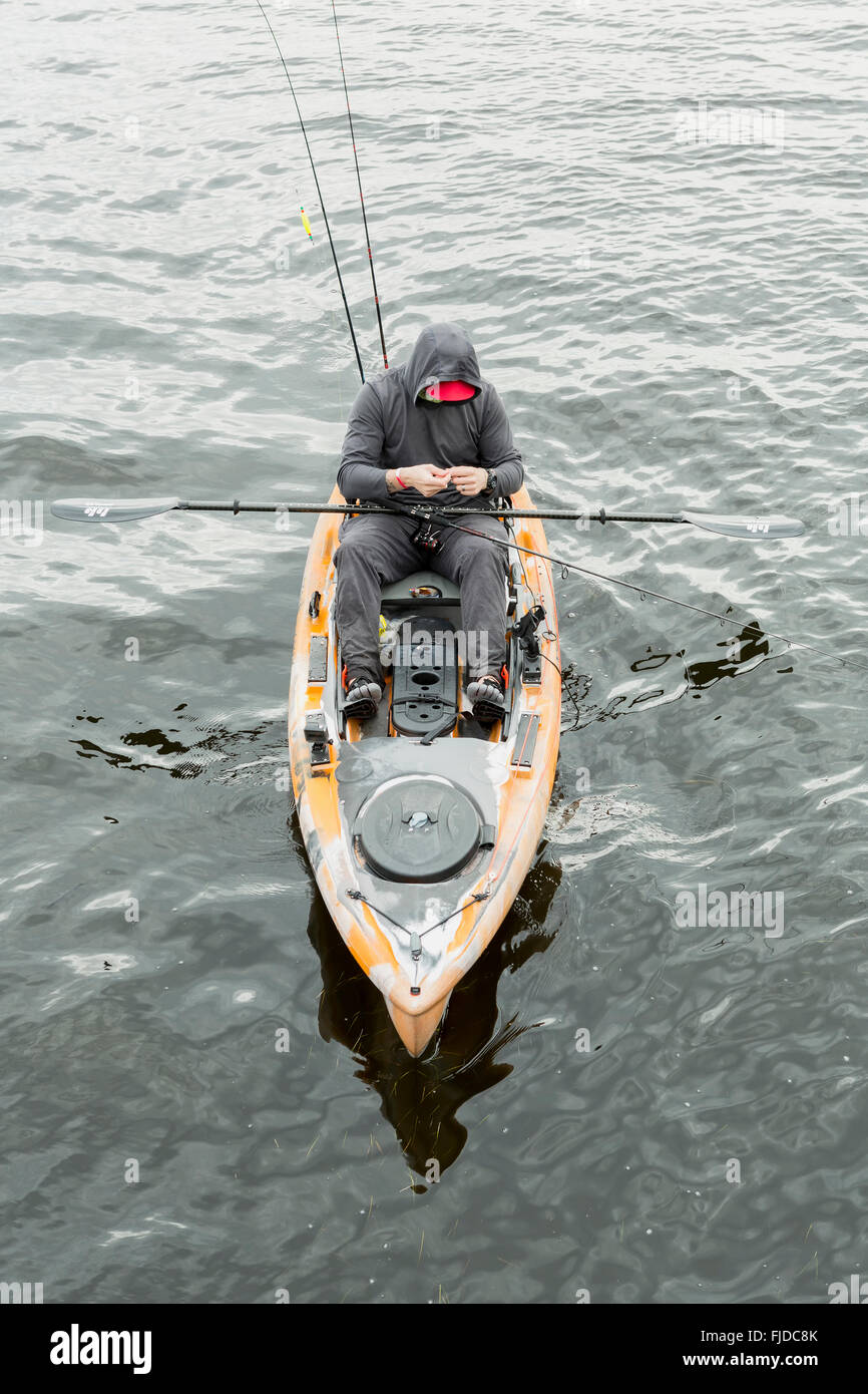 The man in the orange kayak to catch fish. He wears a black hood. Man fishing from a kayak in a gloomy day at sea. Stock Photo