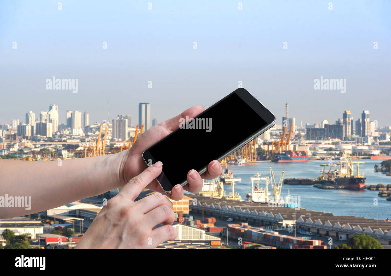 female hand hold and touch screen smart phone, tablet,cellphone over blurred tall yellow industrial cranes Stock Photo