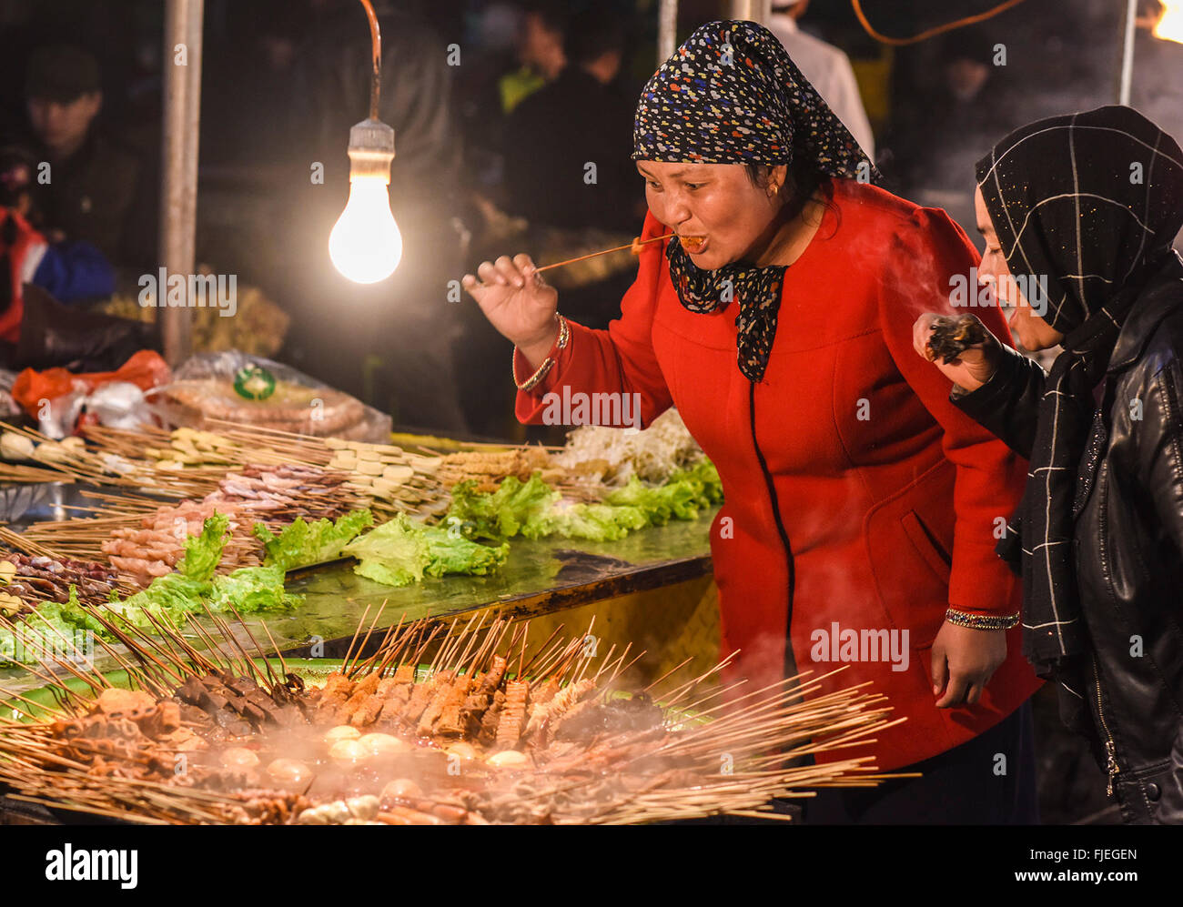 (160302) -- BACHU, March 2, 2016 (Xinhua) -- Women eat local special snacks at a night market in Bachu County of northwest China's Xinjiang Uygur Autonomous Region, March 1, 2016. (Xinhua/Shen Qiao)(wjq) Stock Photo