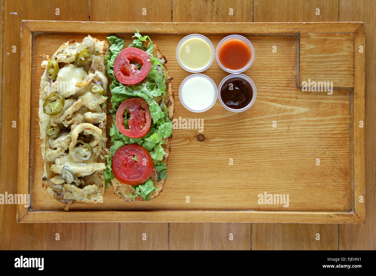 Open face healthy meat and vegetable sandwich served with condiment sauces on a wooden tray