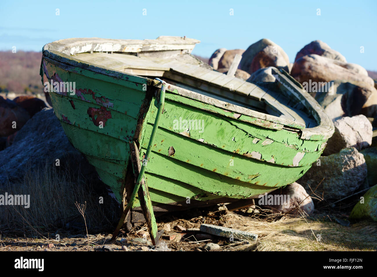 A weathered and gnarled wooden rowboat on land. The boat is painted green. Granite boulders in background. Stock Photo