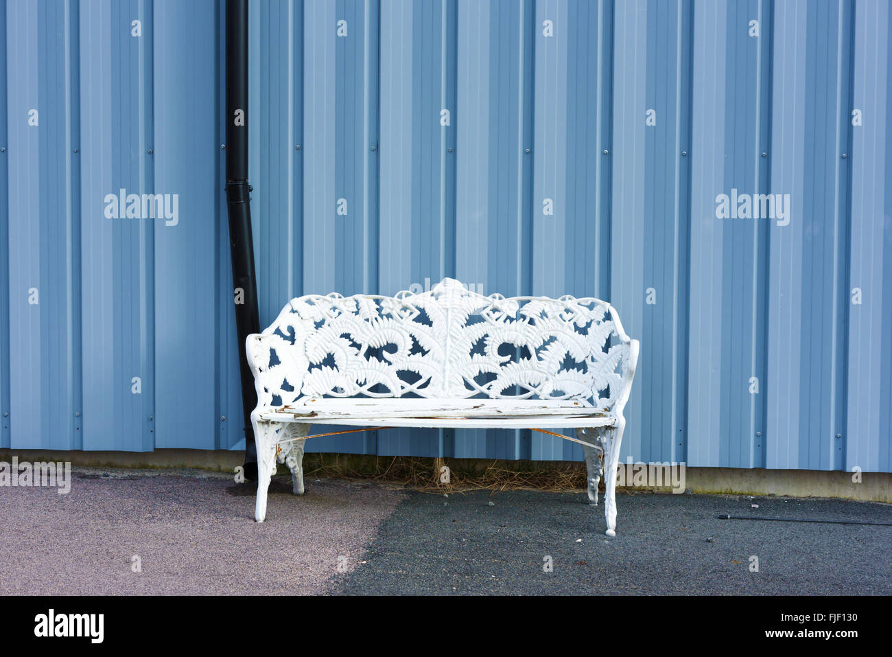 A white empty bench against a bluish gray metal wall. Copy space on wall. Stock Photo
