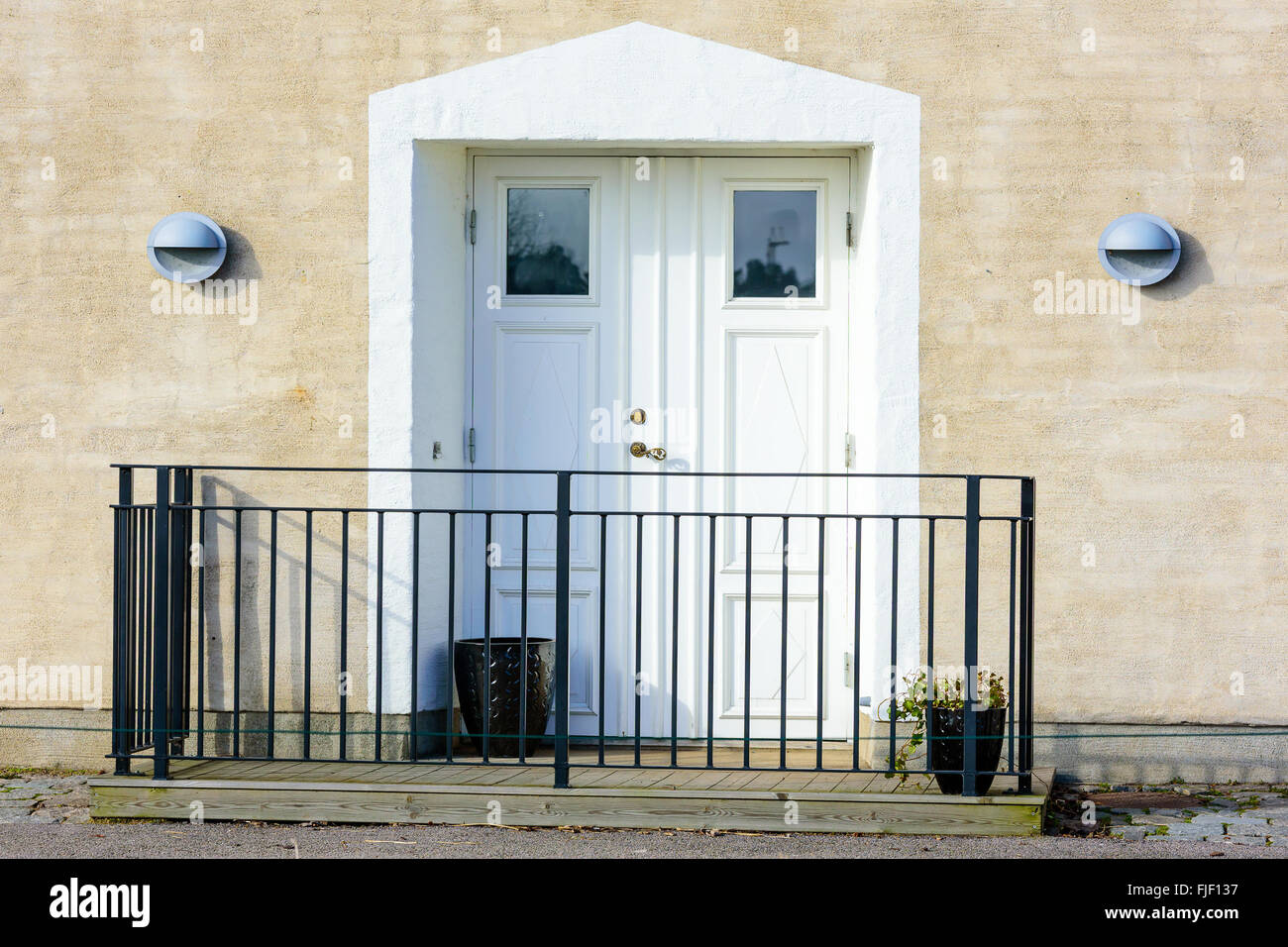 A white door and doorway on a building. Lamps on either side and a metal fence in front. Stock Photo