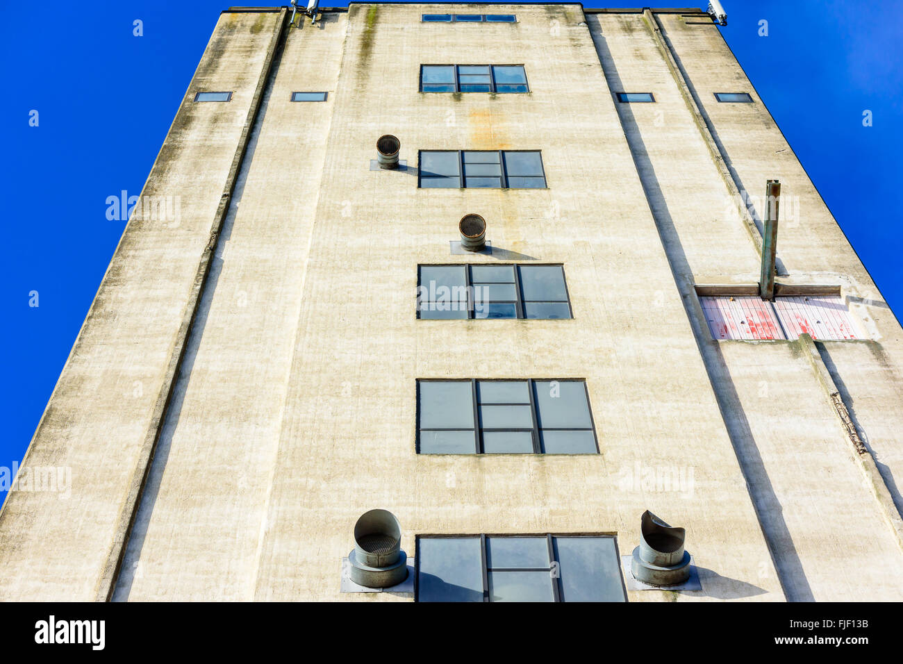 A tall industrial building up close. The abandoned building has some interesting air vents sticking out on the facade. Blue sky Stock Photo