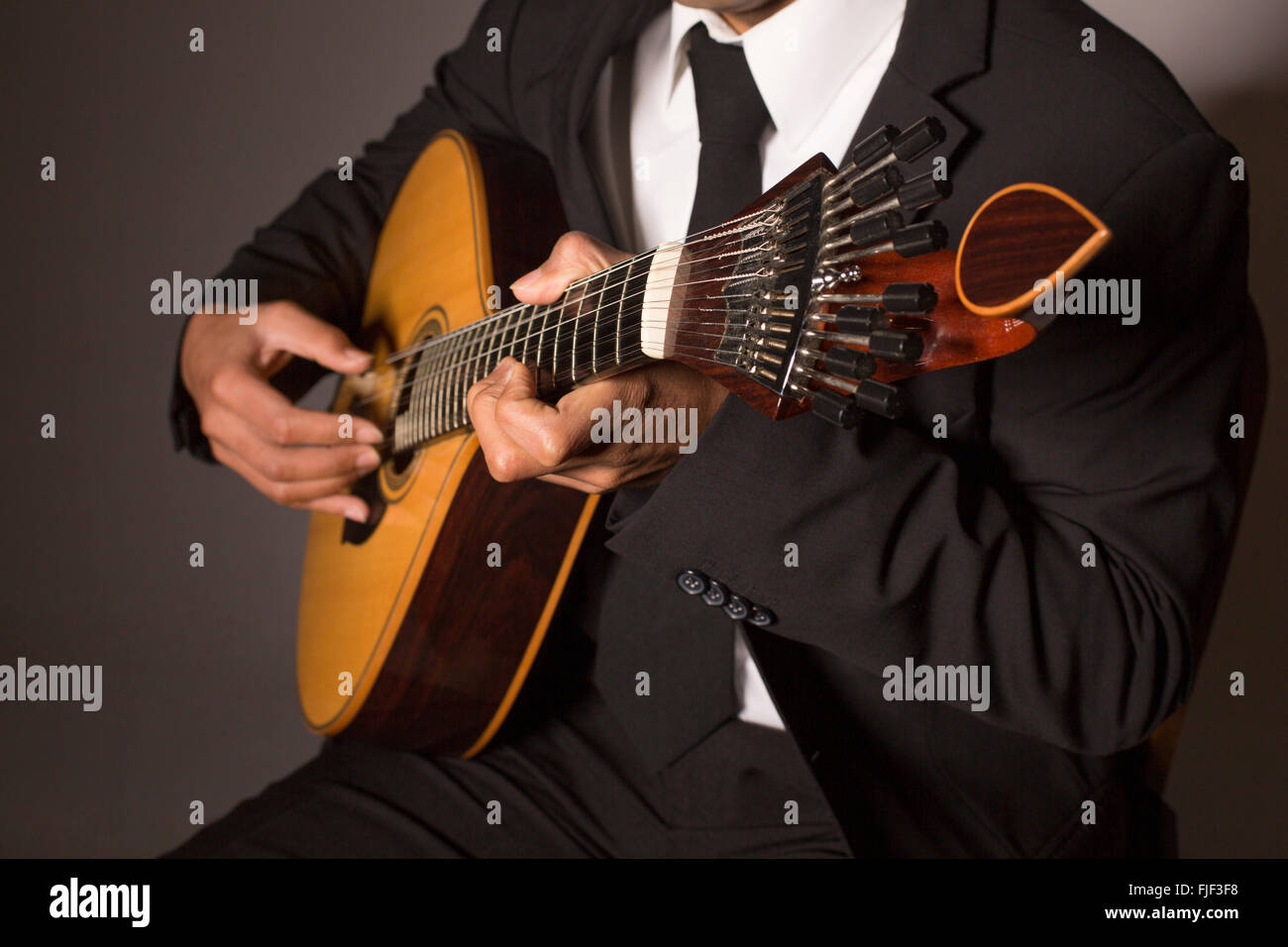 Close up shot of a man with his fingers on the frets of a portuguese guitar playing Stock Photo