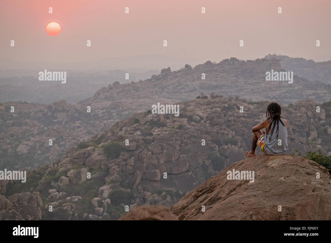 A backpacker contemplates the sunset from a hilltop in Hampi,Karnataka,India Stock Photo