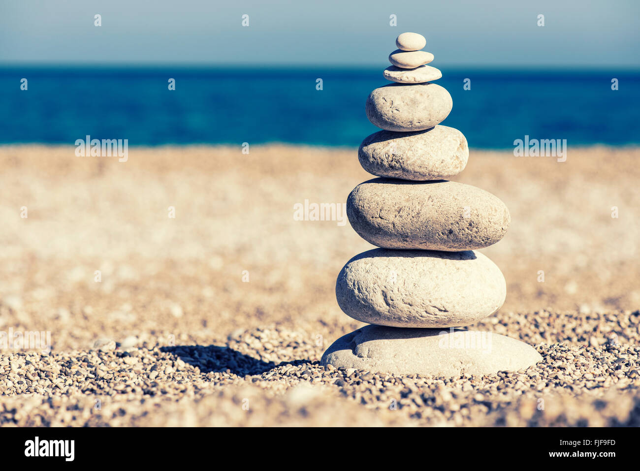 Stones balance, vintage retro instagram like hierarchy stack over blue sea background. Spa or well-being, freedom and stability Stock Photo