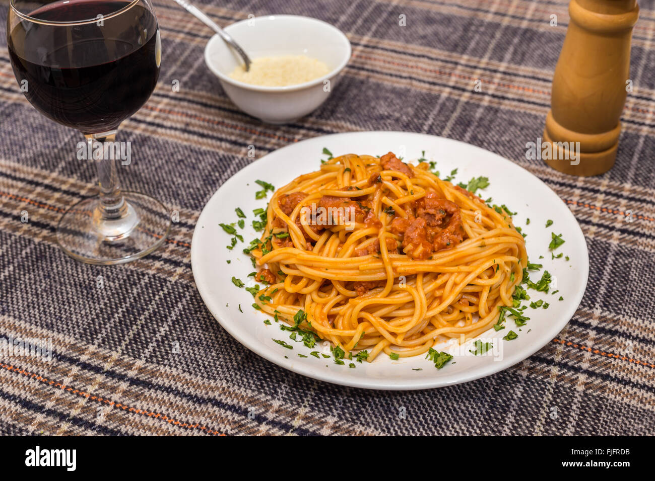 White plate with spagetti bolognese, glass of wine and bowl of parmesan. Stock Photo