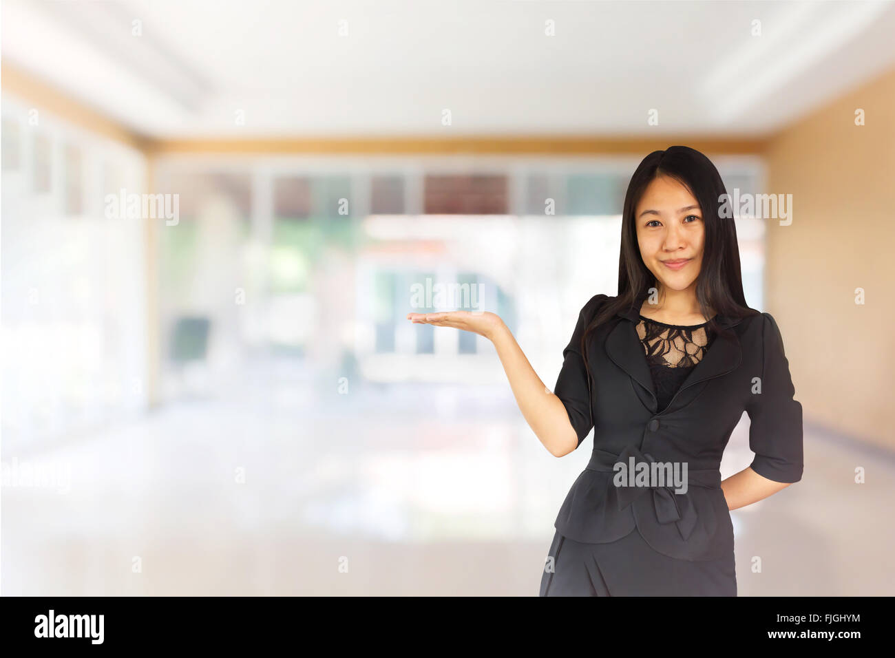 Smiling young Asian business women in black suit holding out hand to show or present space for product and text in home office Stock Photo