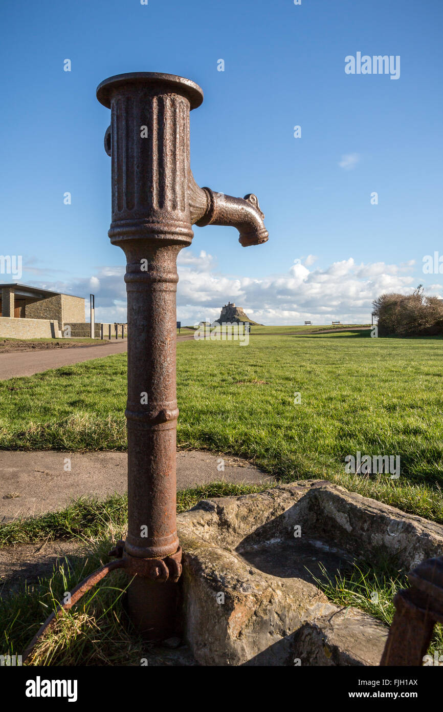 Old water pump with Lindisfarne Castle in distance on Holy Island, Northumberland, England, UK, GB, Europe Stock Photo