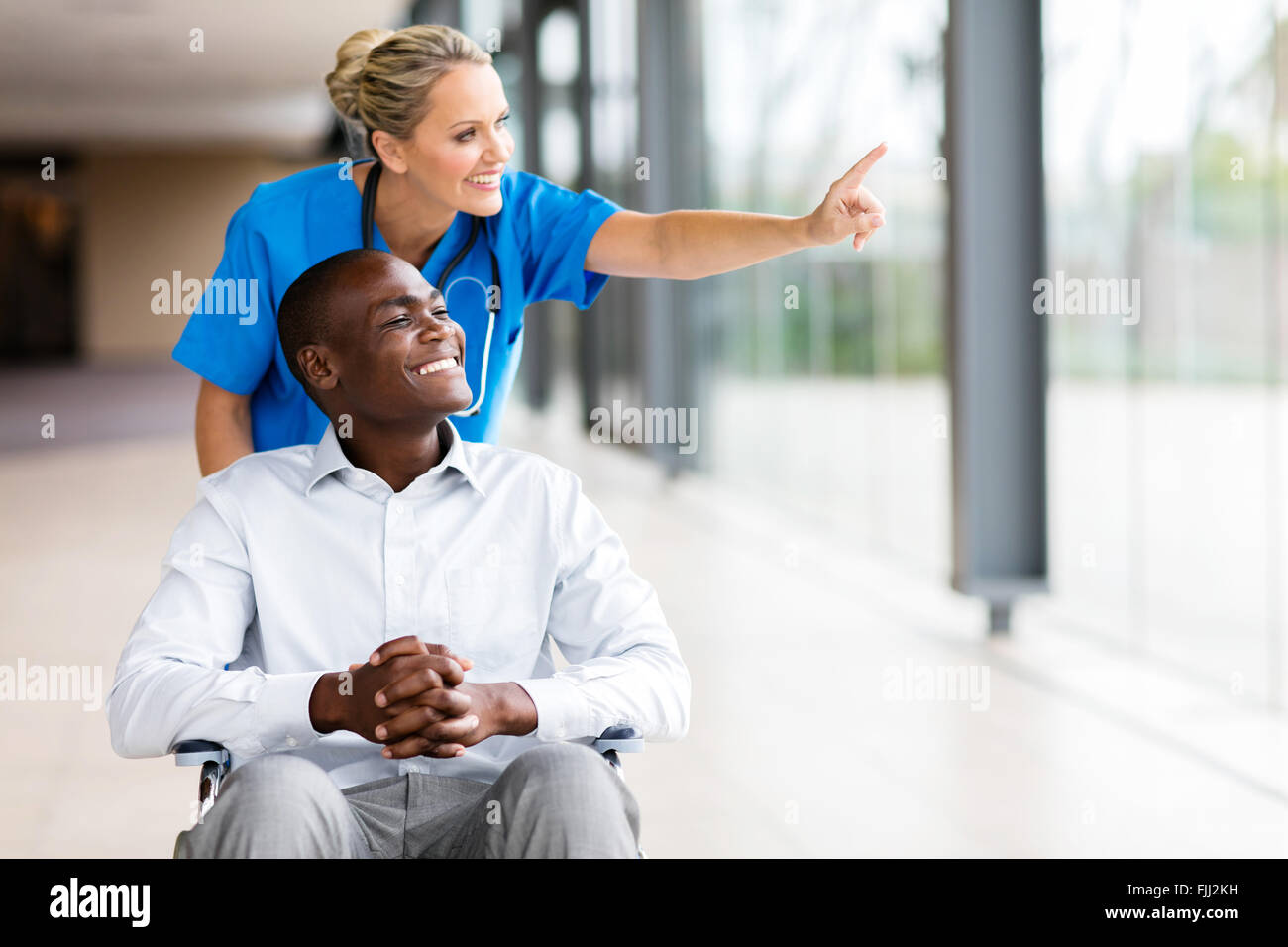 happy healthcare worker taking disabled patient for a walk in hospital Stock Photo