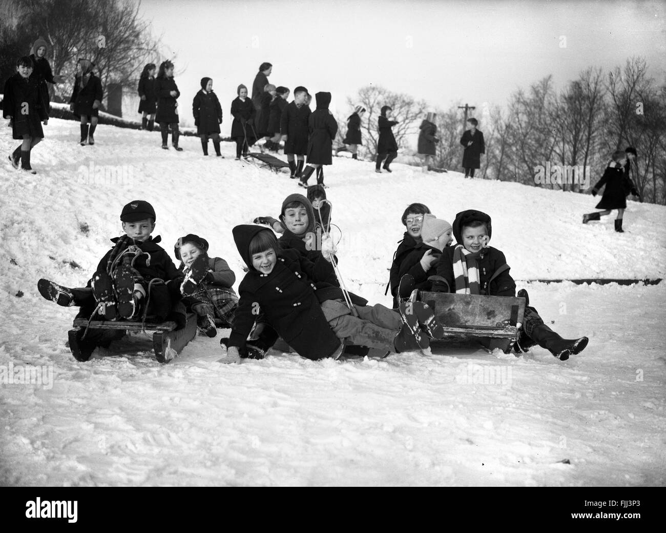 School children sledging and playing in the snow during break time England Britain 1960s winter 1961 playing fun UK Stock Photo