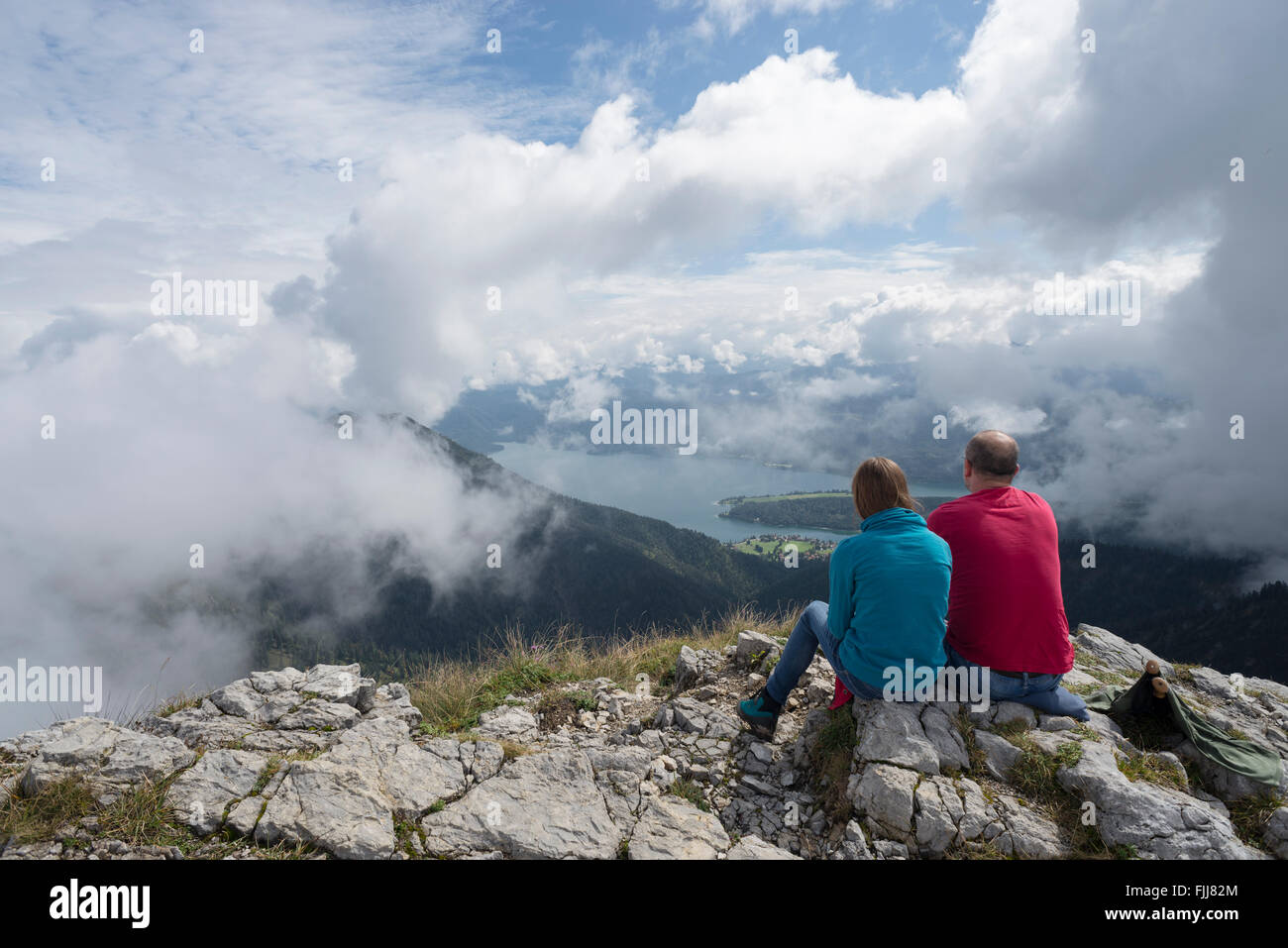 Father and daughter sitting on a mountain summit watching cloud covered scenery at Lake Walchensee, Bavaria, Germany Stock Photo