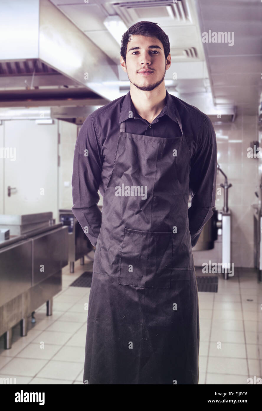 Young chef or waiter posing, wearing black apron and shirt standing in ...