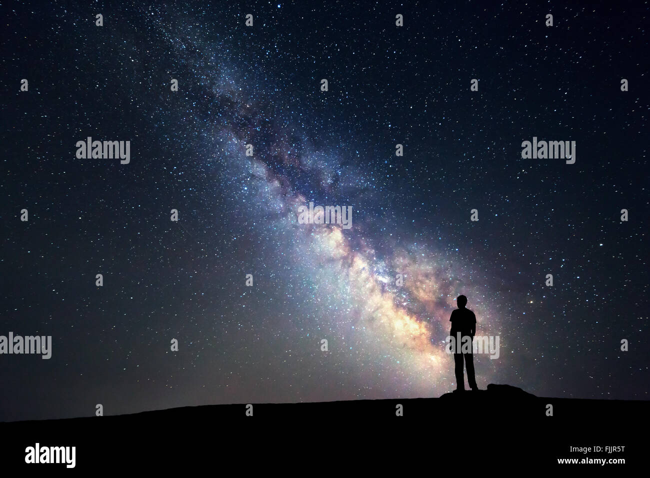 Landscape with Milky Way. Night sky with stars and silhouette of a standing happy man on the mountain. Stock Photo