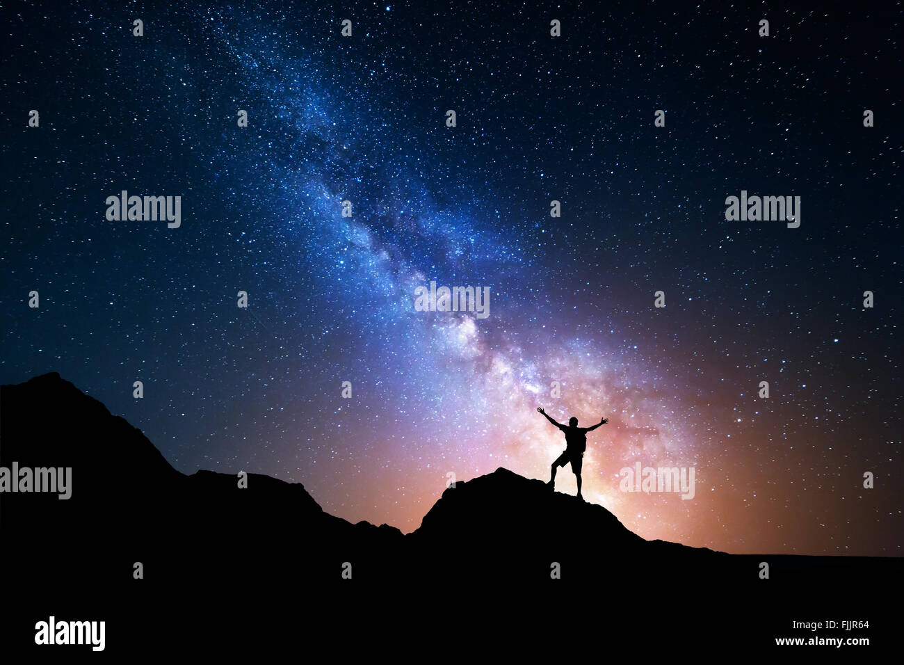 Landscape with Milky Way. Night sky with stars and silhouette of a standing happy man with raised up arms on the mountain. Stock Photo