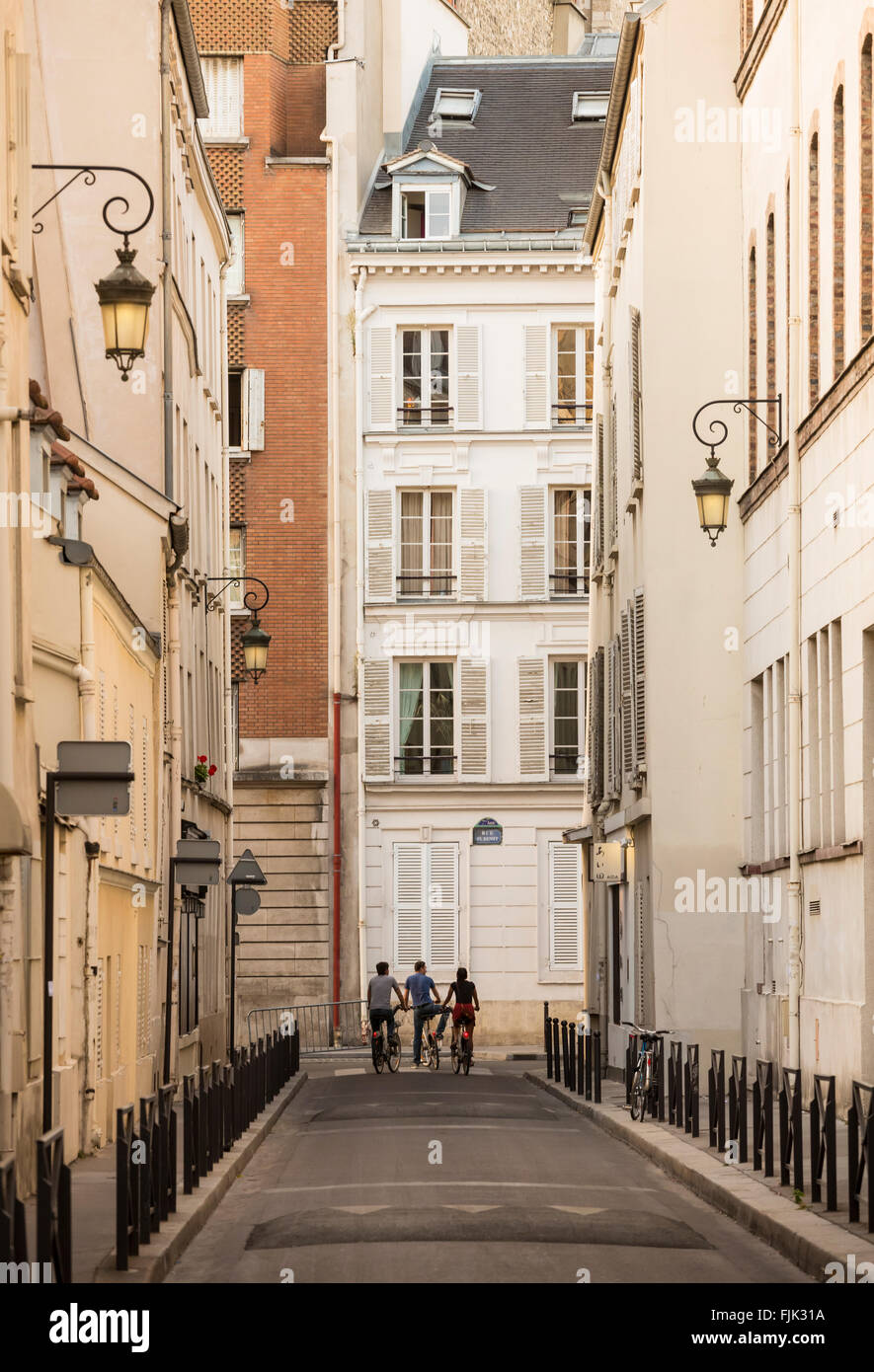 Three bicyclists pause at the end of a narrow street in Paris, France Stock Photo