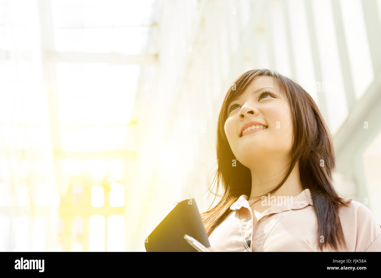 Young Asian business woman smiling and looking up, standing in an ...