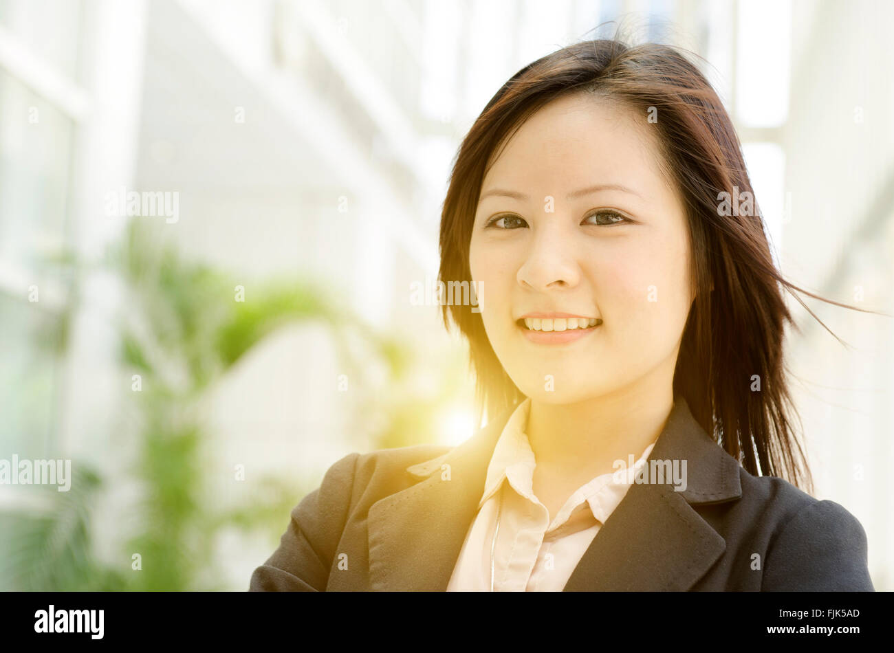 Portrait of a young Asian business woman smiling and standing at an ...