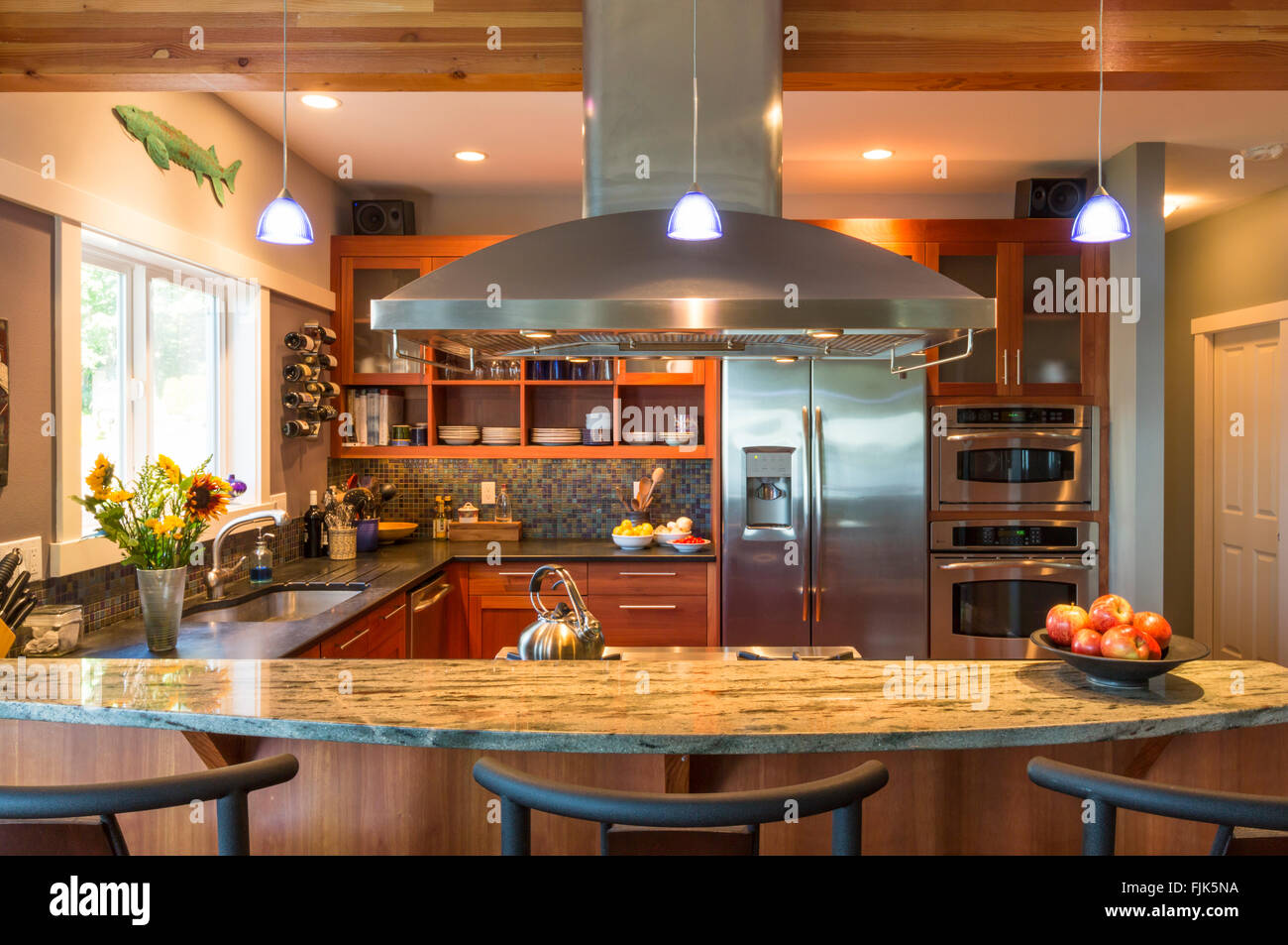 Breakfast bar in contemporary upscale home kitchen with granite countertops, stainless steel appliances and accent lighting Stock Photo