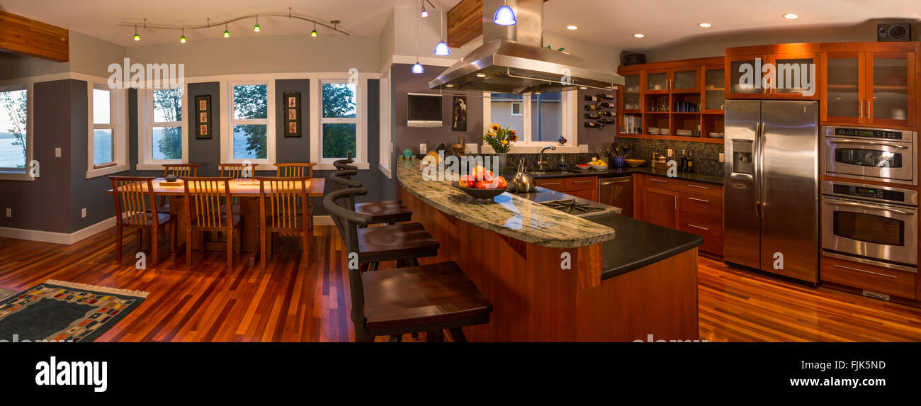 Open plan kitchen & dining area in contemporary upscale home interior with wood cabinets and floors, view windows, appliances and breakfast bar Stock Photo