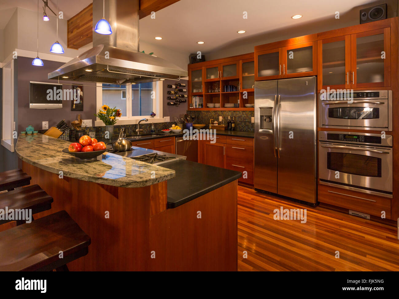 Contemporary upscale home kitchen interior with wood cabinets & floors, granite countertops, stainless steel appliances and accent lighting Stock Photo