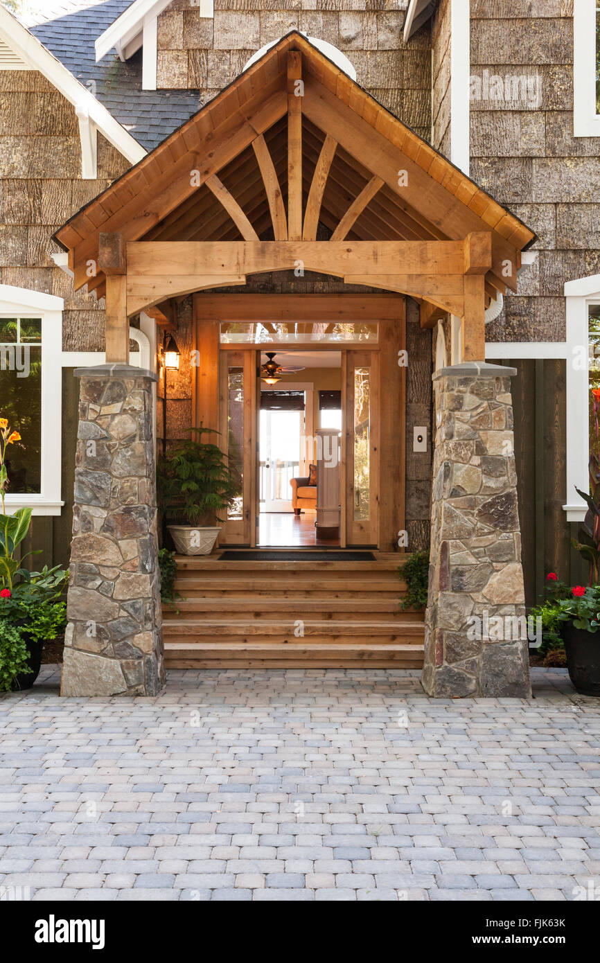 Home exterior with wood and stone porch, open front door and paving stone driveway. Entryway facade of luxury upscale Craftsman style country house. Stock Photo