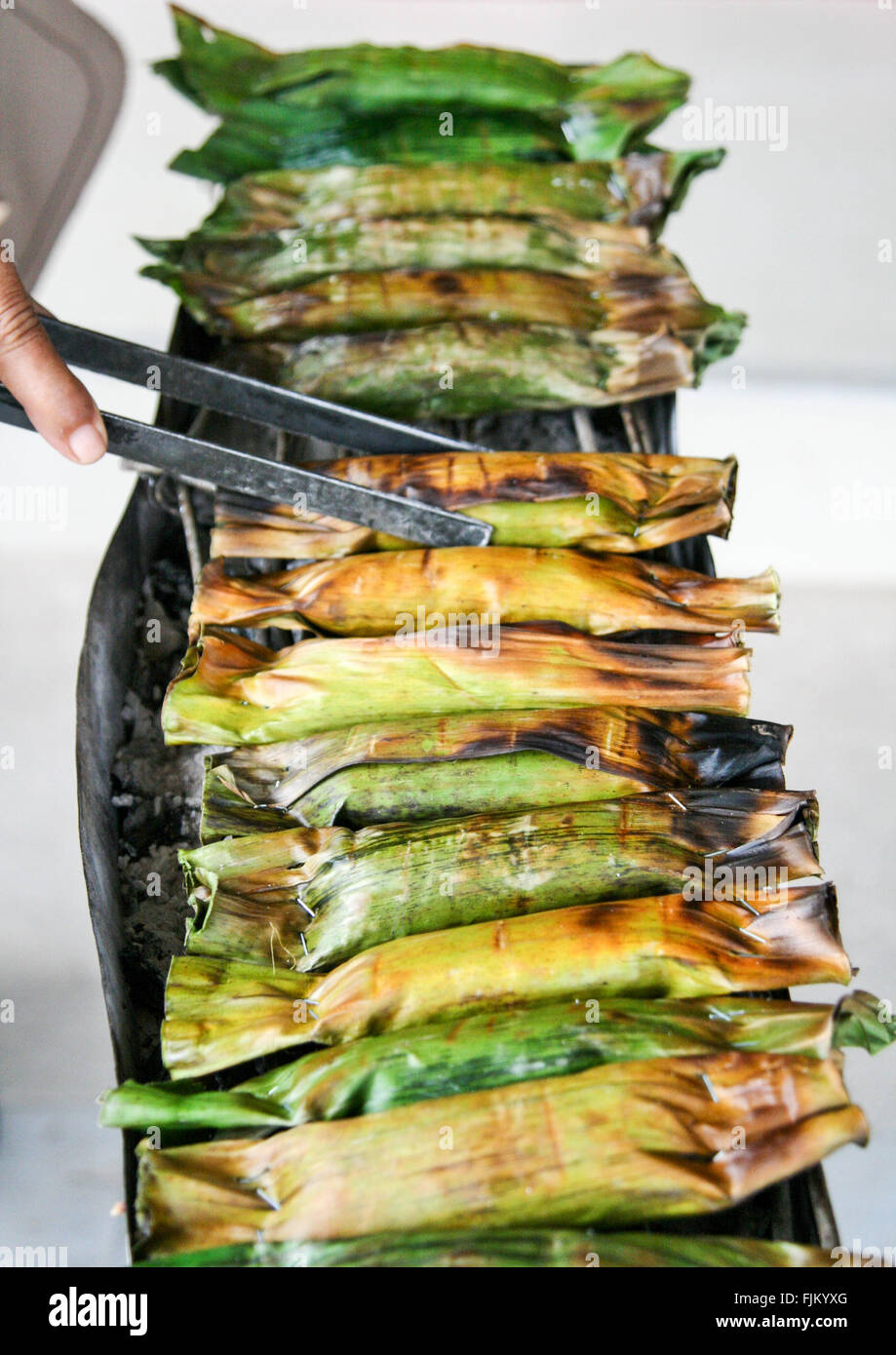 Woman cooking sticky rice wrapped in banana leaves on a market stall in Khao Sok, Thailand Stock Photo