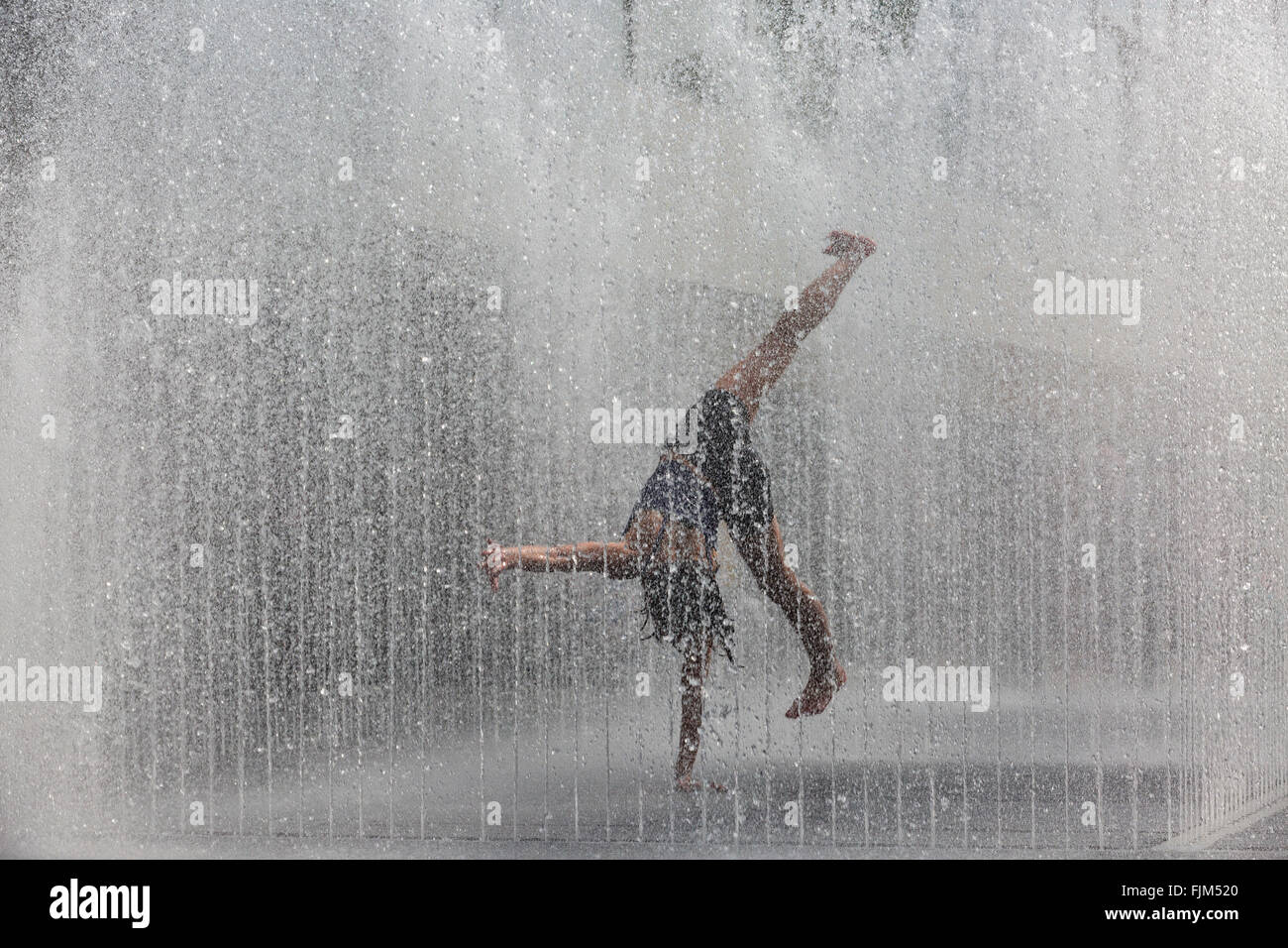 Teenage girl doing cartwheels among the curtains of the Appearing Rooms fountains at the Royal Festival Hall, Southbank, London, UK Stock Photo