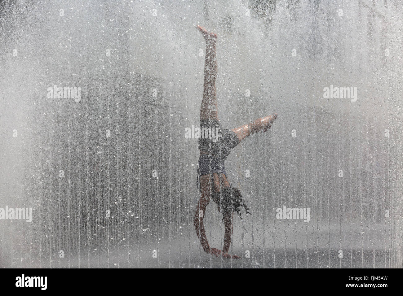 Teenage girl doing cartwheels among the curtains of water at the Appearing Rooms fountains at the Royal Festival Hall, Southbank, London, UK Stock Photo