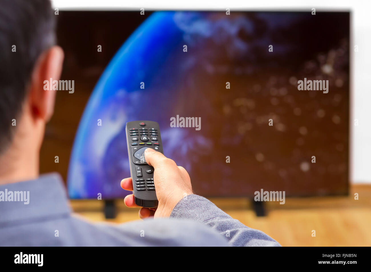 Man sitting on a sofa watching tv holding remote control. Focus on the remote control. Stock Photo