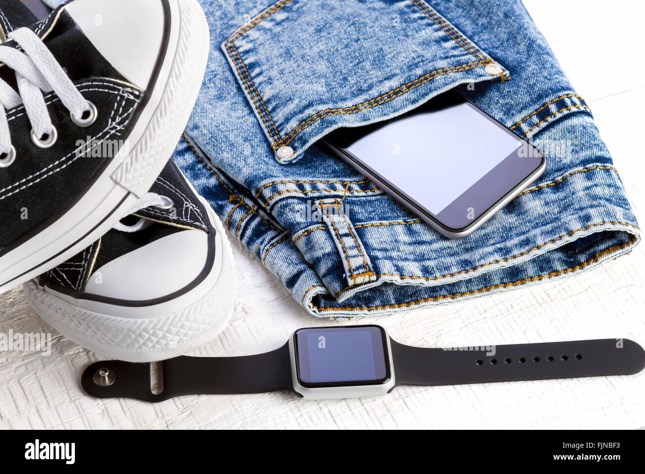 Smartphone, smartwatch, jeans and sport shoes on white wooden boards. Stock Photo