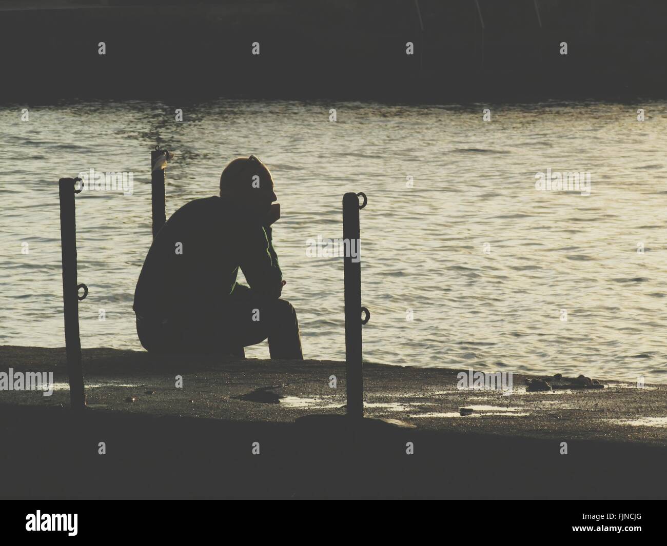 Rear View Of Man Sitting On Pier By Lake Stock Photo