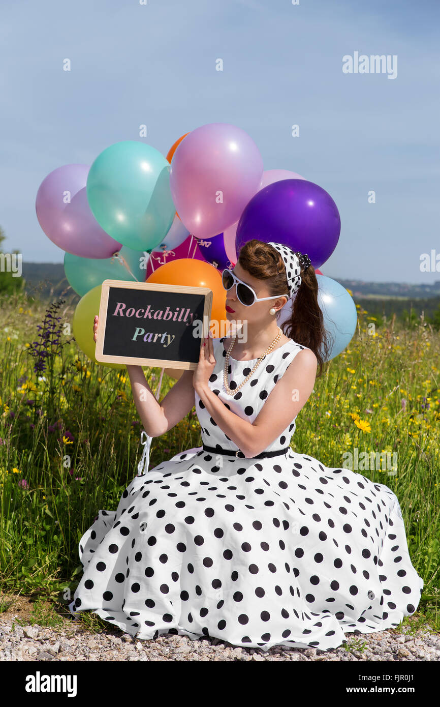 beautiful woman with a petticoat dress holding a slate with text Rockabilly Party, concept invitation und party Stock Photo