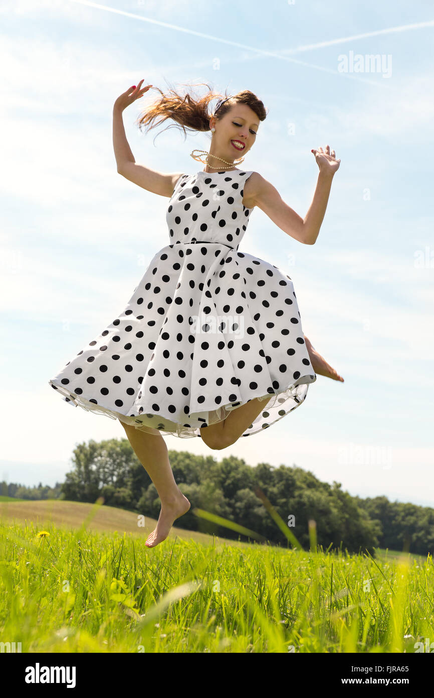 Pin up Girl with white petticoat dress is jumping in the meadow Stock Photo