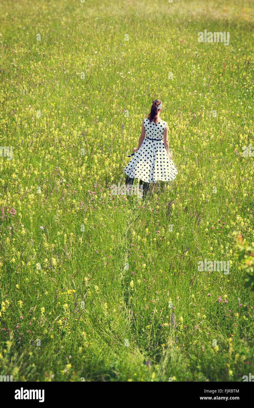 Rockabilly Girl with a white petticoat dress walking through a wildflower meadow, backview Stock Photo